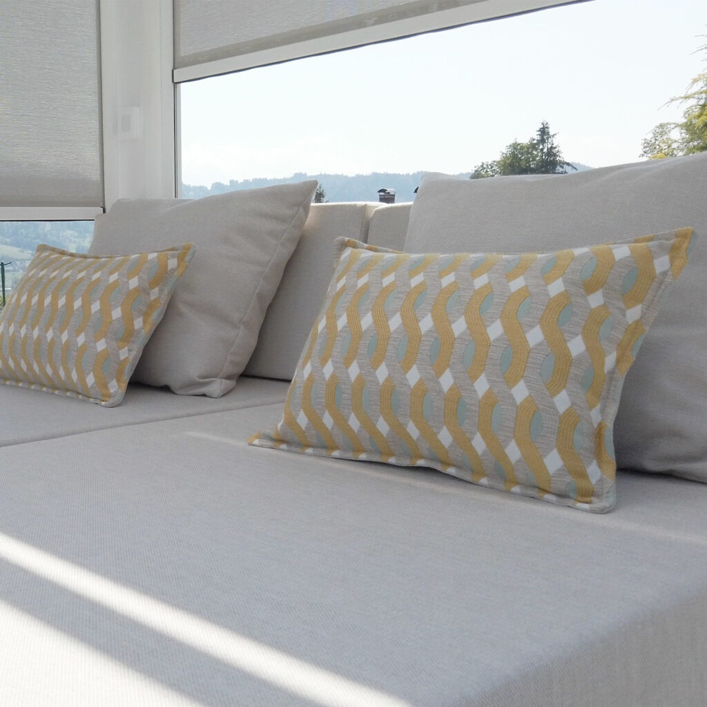 Zoom sur les oreillers dont les motifs de tissus sont très décoratifs, les stores en arrière plan sont entre-ouverts